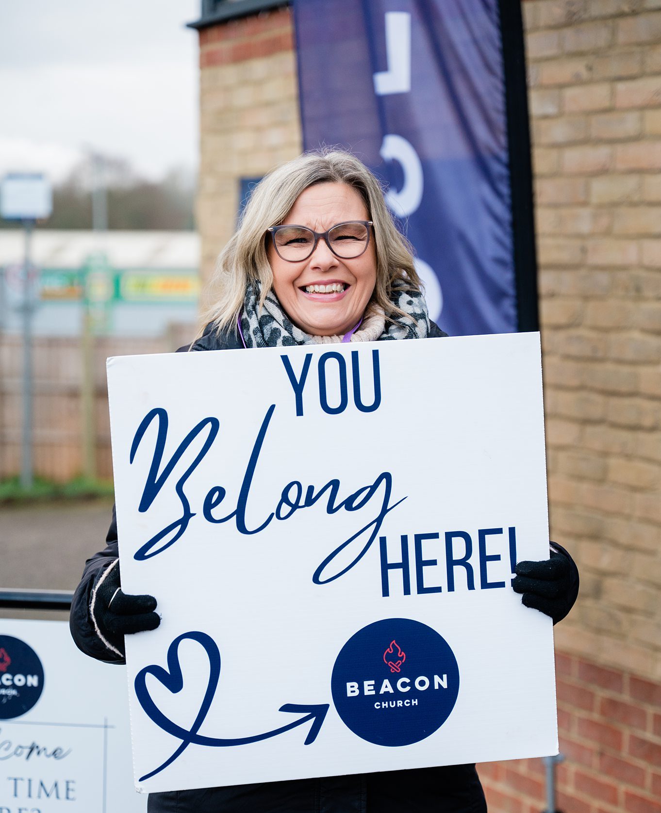 “Woman holding a ‘You belong here’ welcome sign outside a church in Bury St Edmunds, Suffolk”