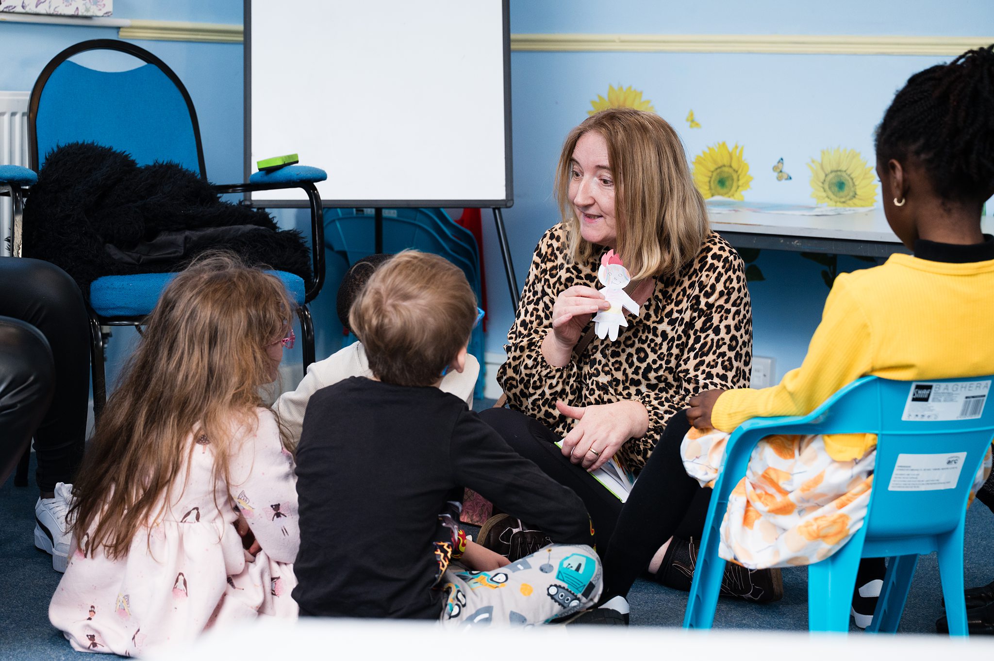 Church children’s group in Bury St Edmunds, Suffolk, with a leader engaging kids in a story and craft activity in a classroom setting.