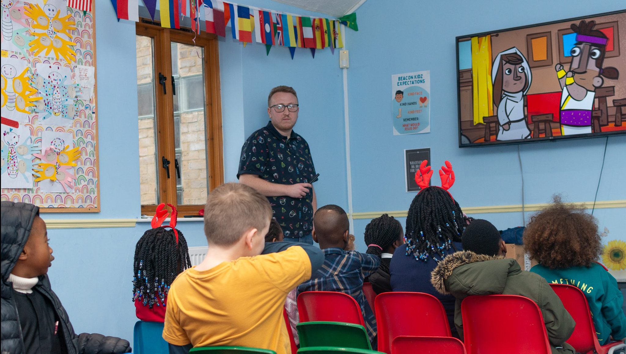 Children watching a Bible story during a kids church session in Bury St Edmunds, Suffolk, with a leader teaching at the front of the classroom.
