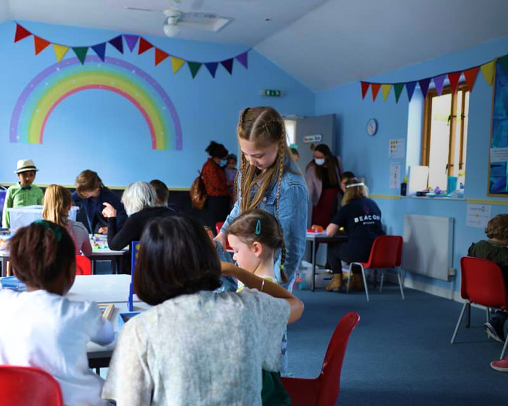Children taking part in a church kids ministry session in Bury St Edmunds, Suffolk, with leaders helping at activity tables in a bright classroom.