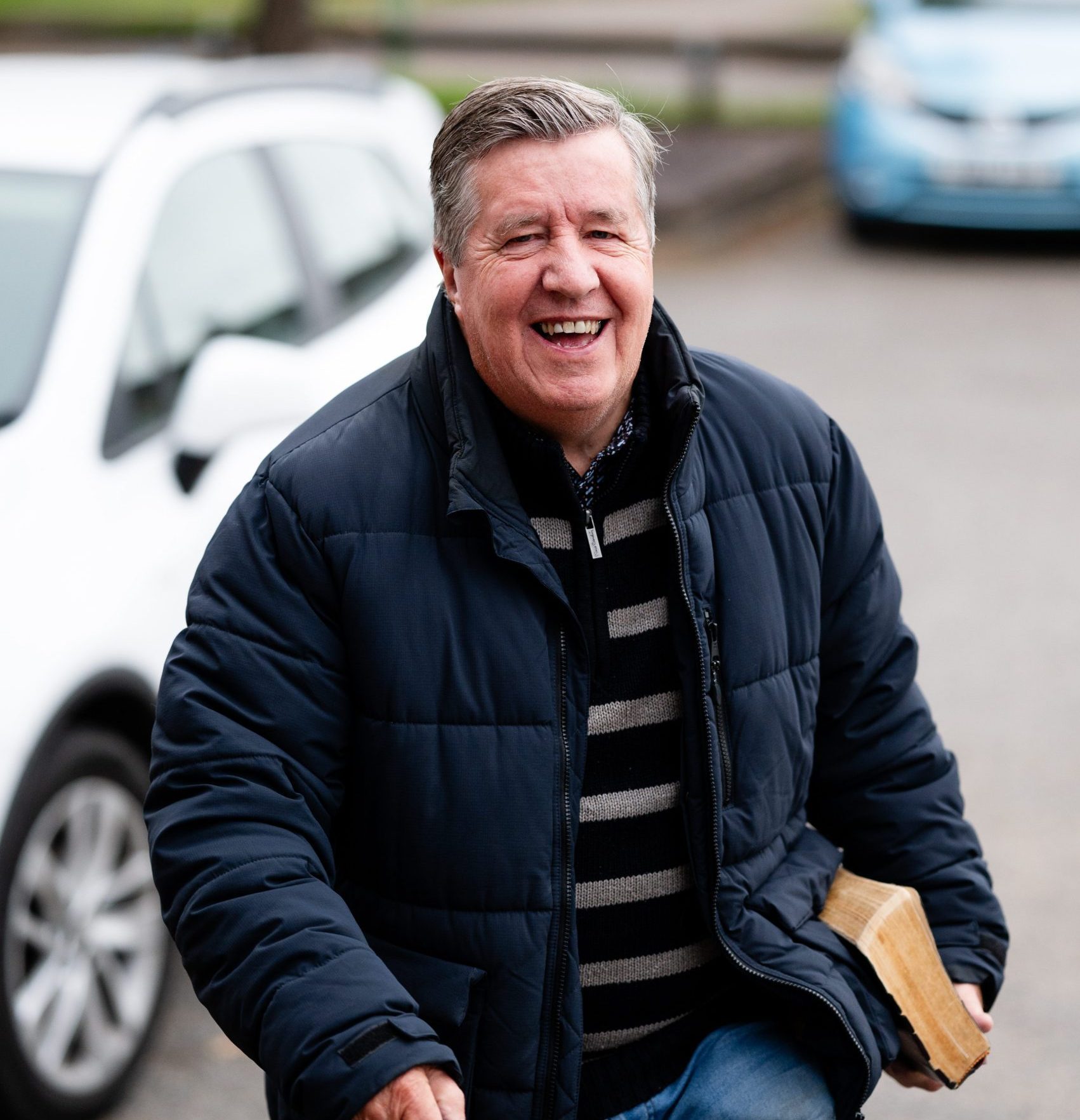 A smiling man arriving at church in Bury St Edmunds, Suffolk, holding a Bible.