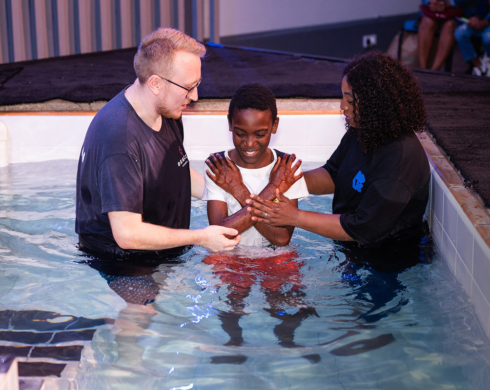 “Person being baptised in water surrounded by church leaders during a service in Bury St Edmunds, Suffolk”
