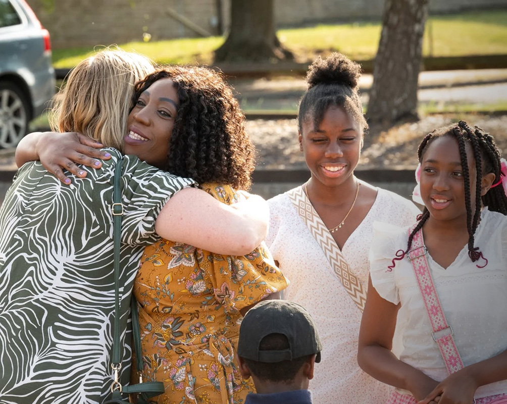 “Women sharing a warm hug while others smile outside a church in Bury St Edmunds, Suffolk”
