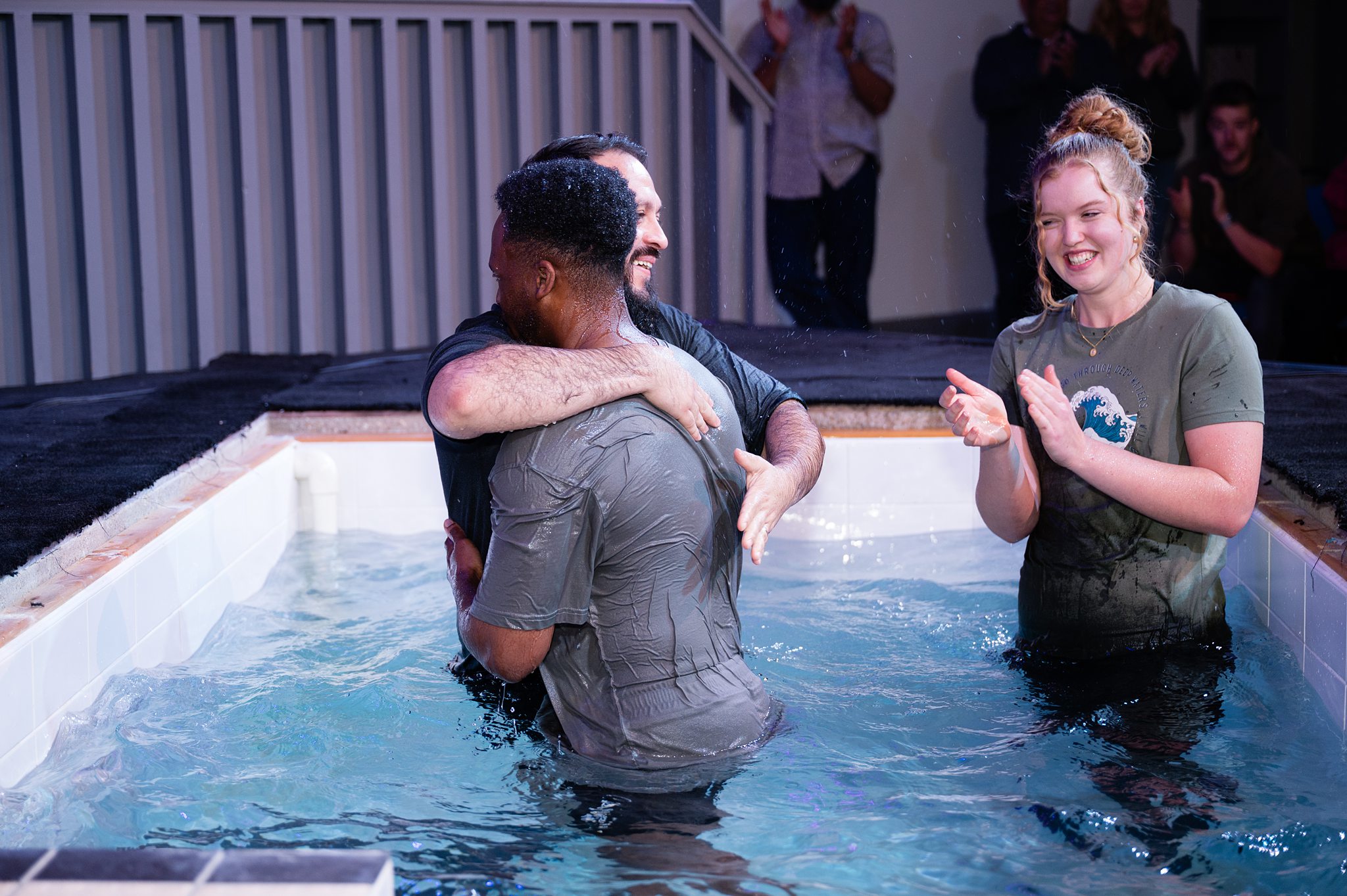 A baptism celebration at Beacon Church in Bury St Edmunds, Suffolk, as a church member embraces another after being baptised, surrounded by a supportive faith community.